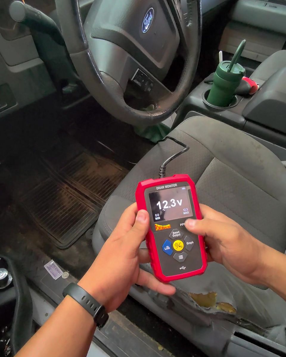 A handheld tester showing a 12.3 V reading inside a vehicle cab