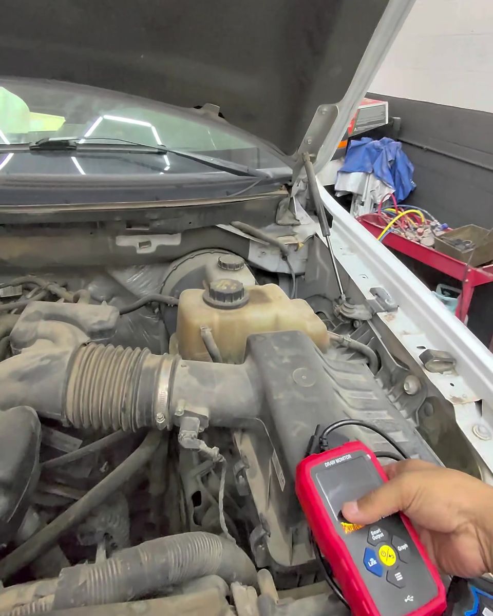 A handheld electrical tester held over an open engine bay